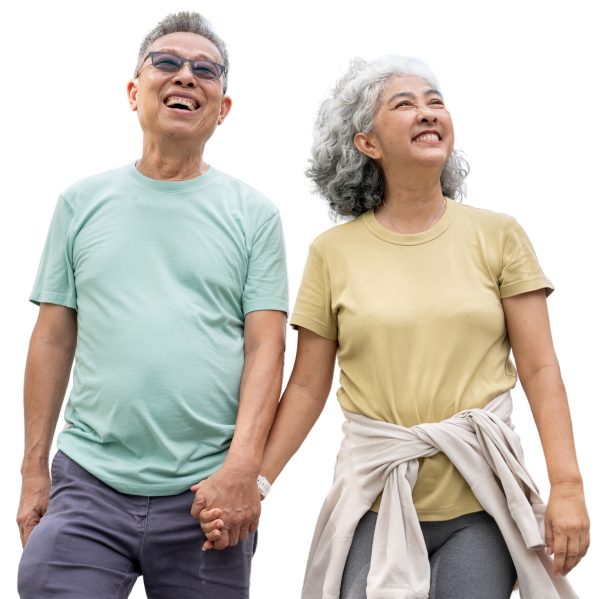 An older couple stands smiling and holding hands. Despite his hearing loss, the man looks happy and relaxed in glasses and a light green t-shirt, while the woman in a yellow shirt with a sweater tied around her waist beams beside him.